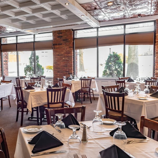 Ciro's Italian restaurant dining room with set tables, dark wood chairs, and large windows.