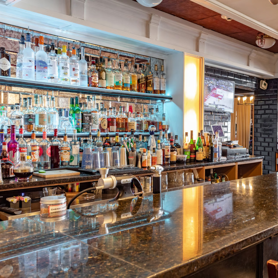 A well-stocked bar at Ciro's with numerous liquor bottles, bar tools, and a dark granite countertop.