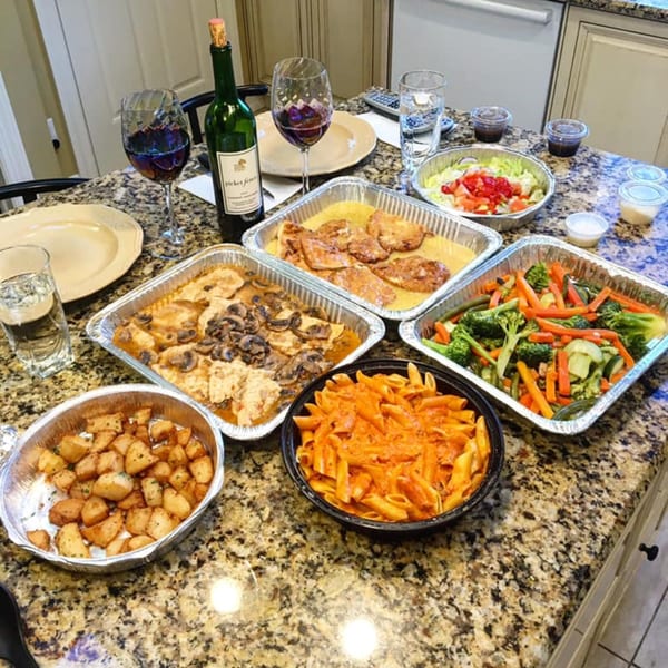 Ciro's Italian takeout feast with pasta, chicken, vegetables, potatoes, salad, and wine on a granite counter.